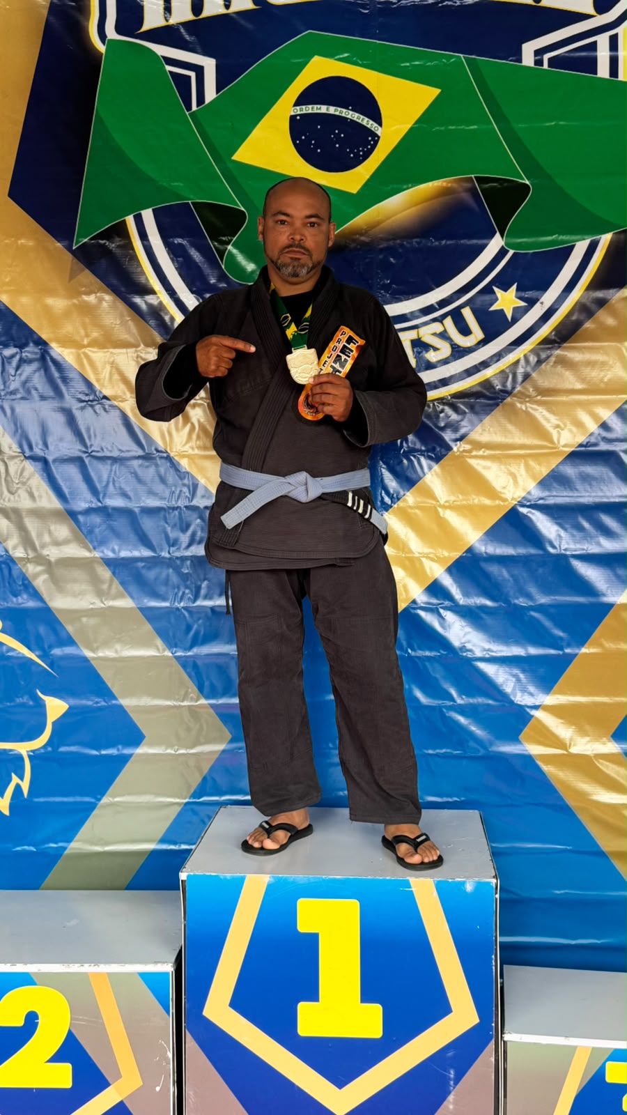Aluno adulto faixa azul no topo do pódio com medalha de ouro