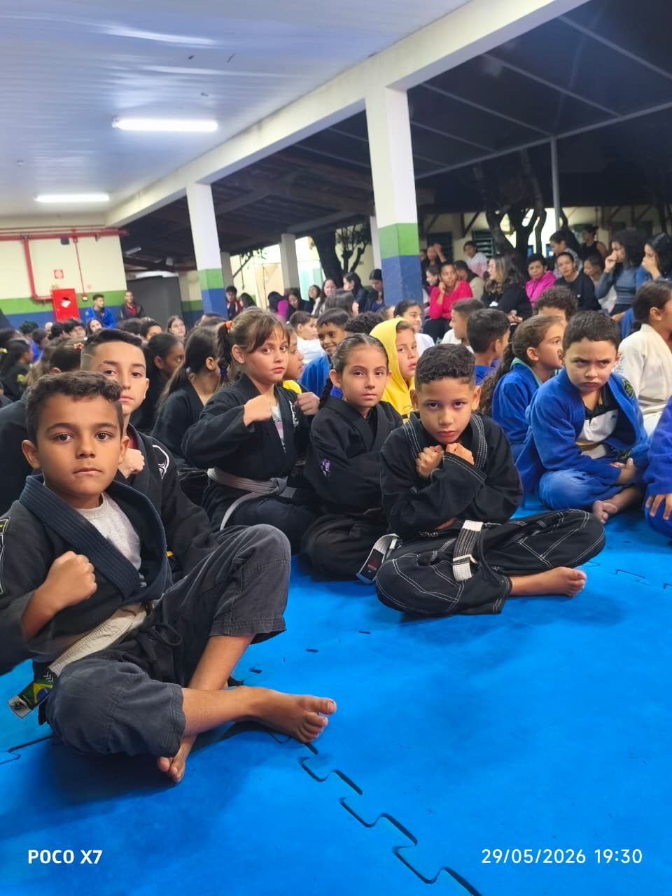 Crianças sentadas no tatame durante cerimônia do projeto
