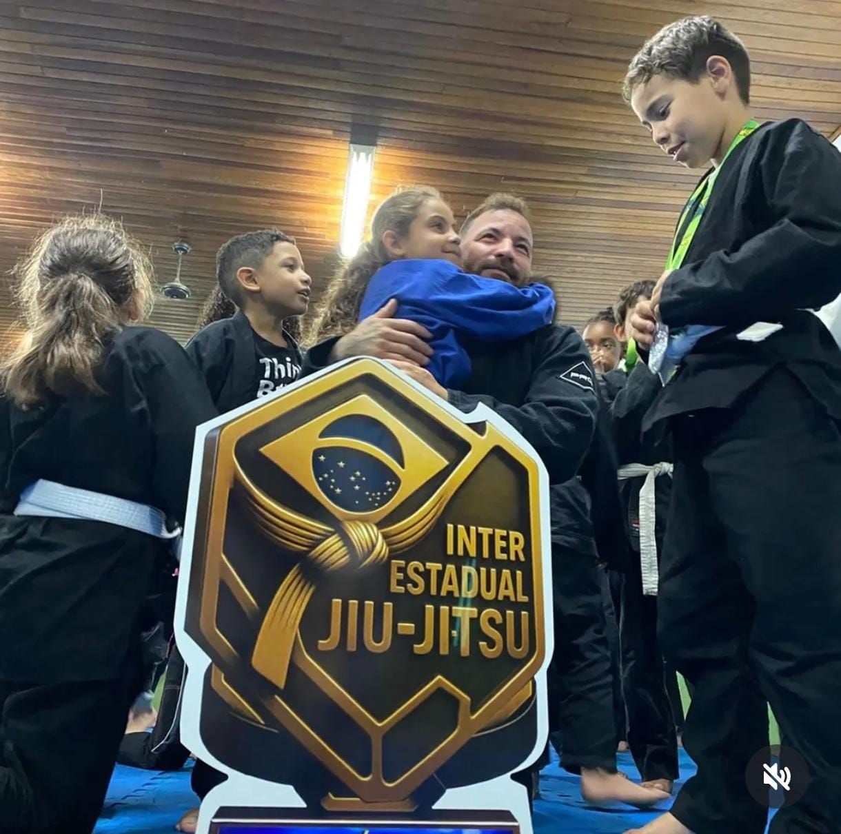 Professor abraçando aluna kids ao lado do troféu Interestadual de Jiu-Jitsu