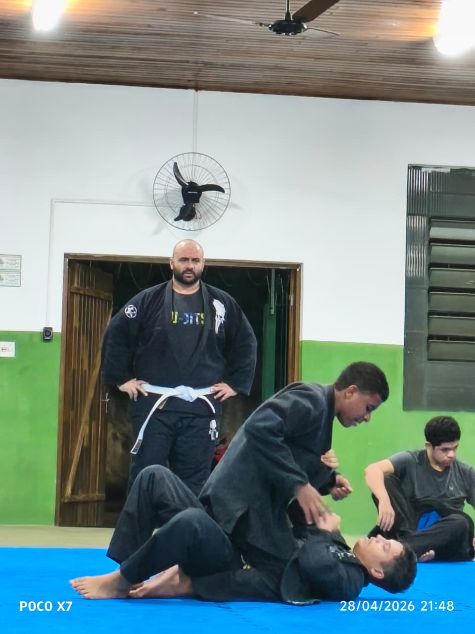 Professor faixa branca observa alunos kids treinando no tatame