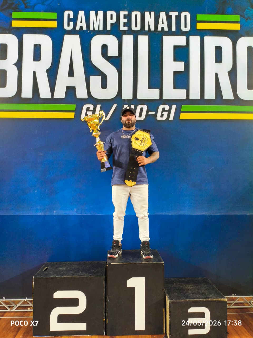 Atleta campeão brasileiro no pódio com troféu e cinturão