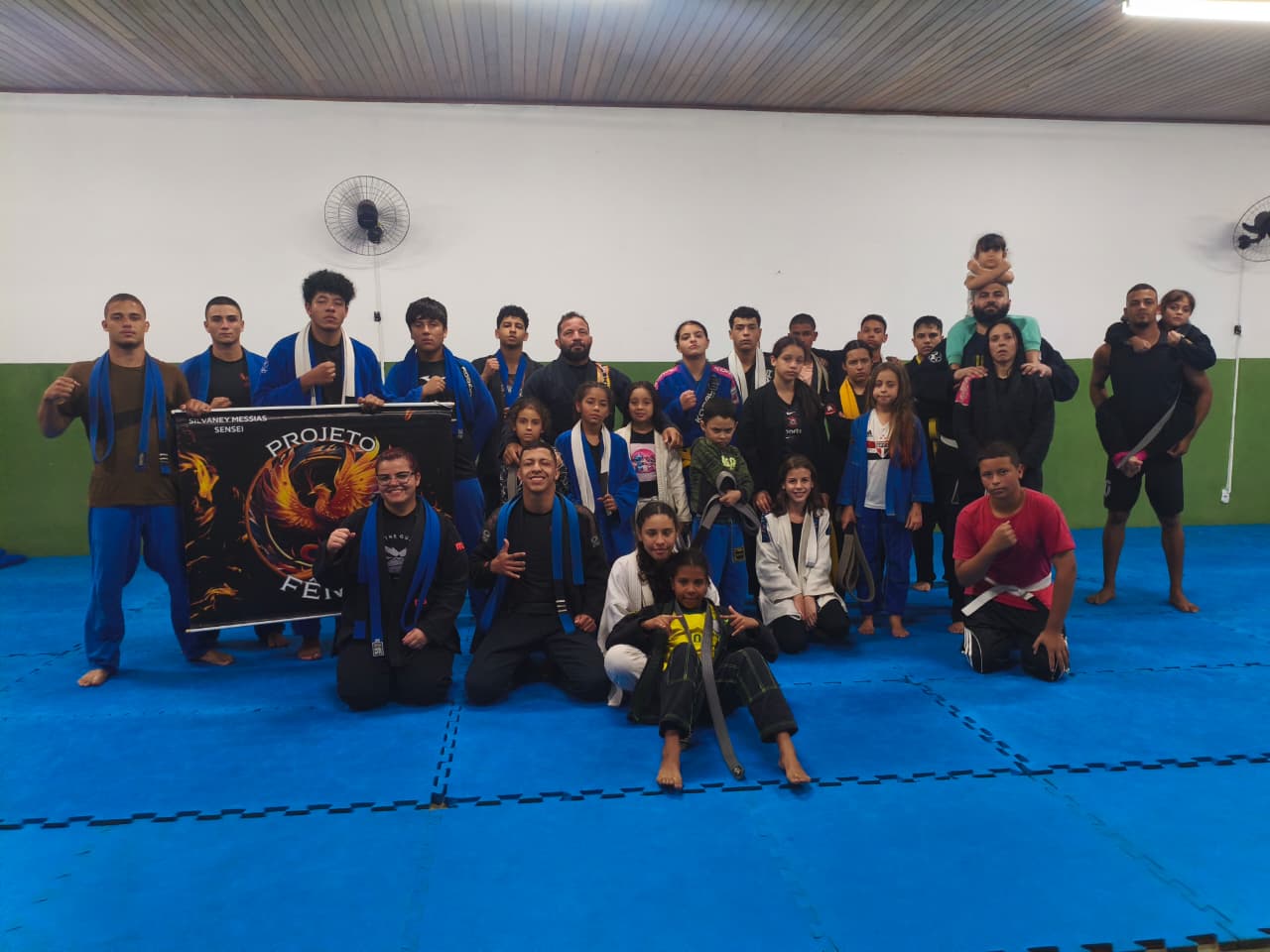 Equipe Projeto Fênix posando ao lado do banner oficial no tatame