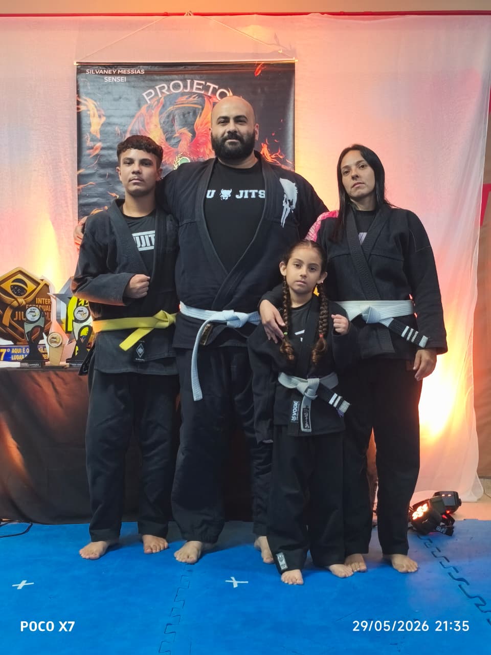Família de atletas posando ao lado dos troféus e do banner Projeto Fênix