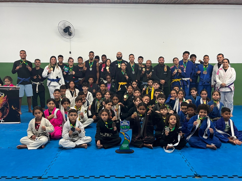 Equipe reunida no tatame com troféus e medalhas do Projeto Fênix